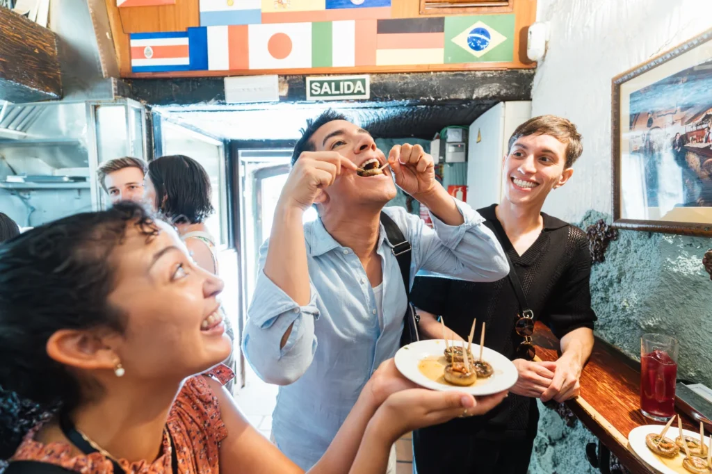 Food tour guests tasting stuffed mushroom tapas at a Madrid bar decorated with international flags on the Tipsy Tapas Tour