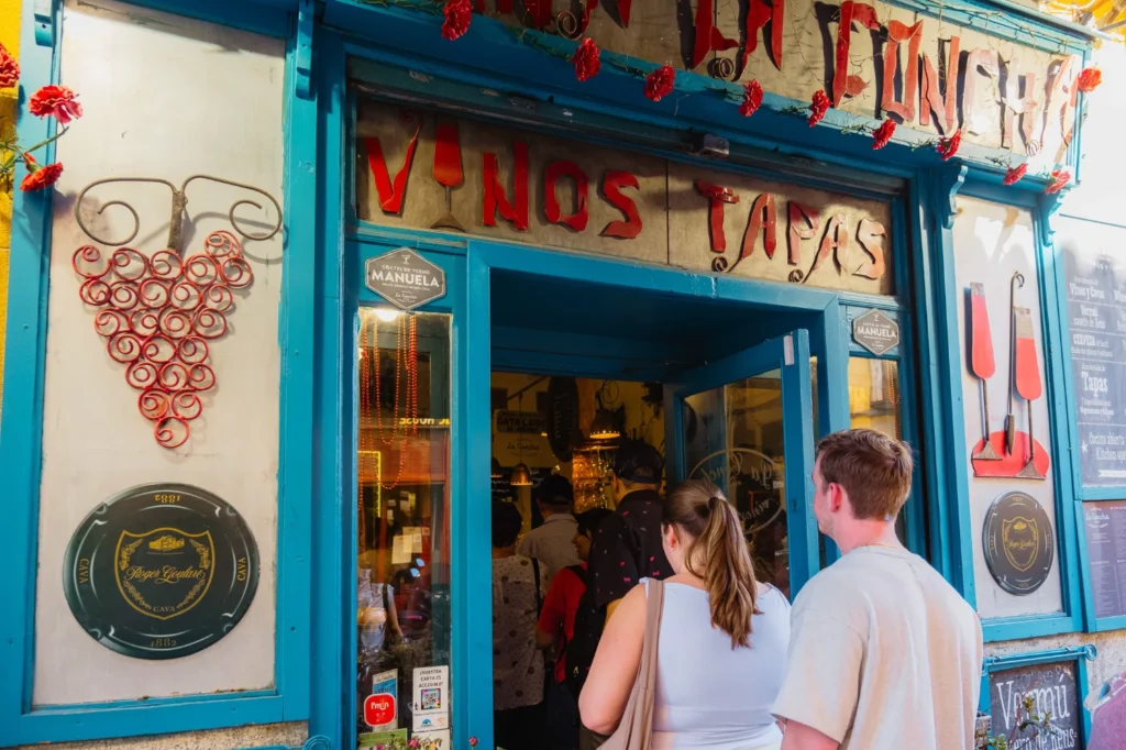 Guests entering a colorful Vinos y Tapas bar with blue facade and decorative grape motif on the Tipsy Tapas Tour of Madrid